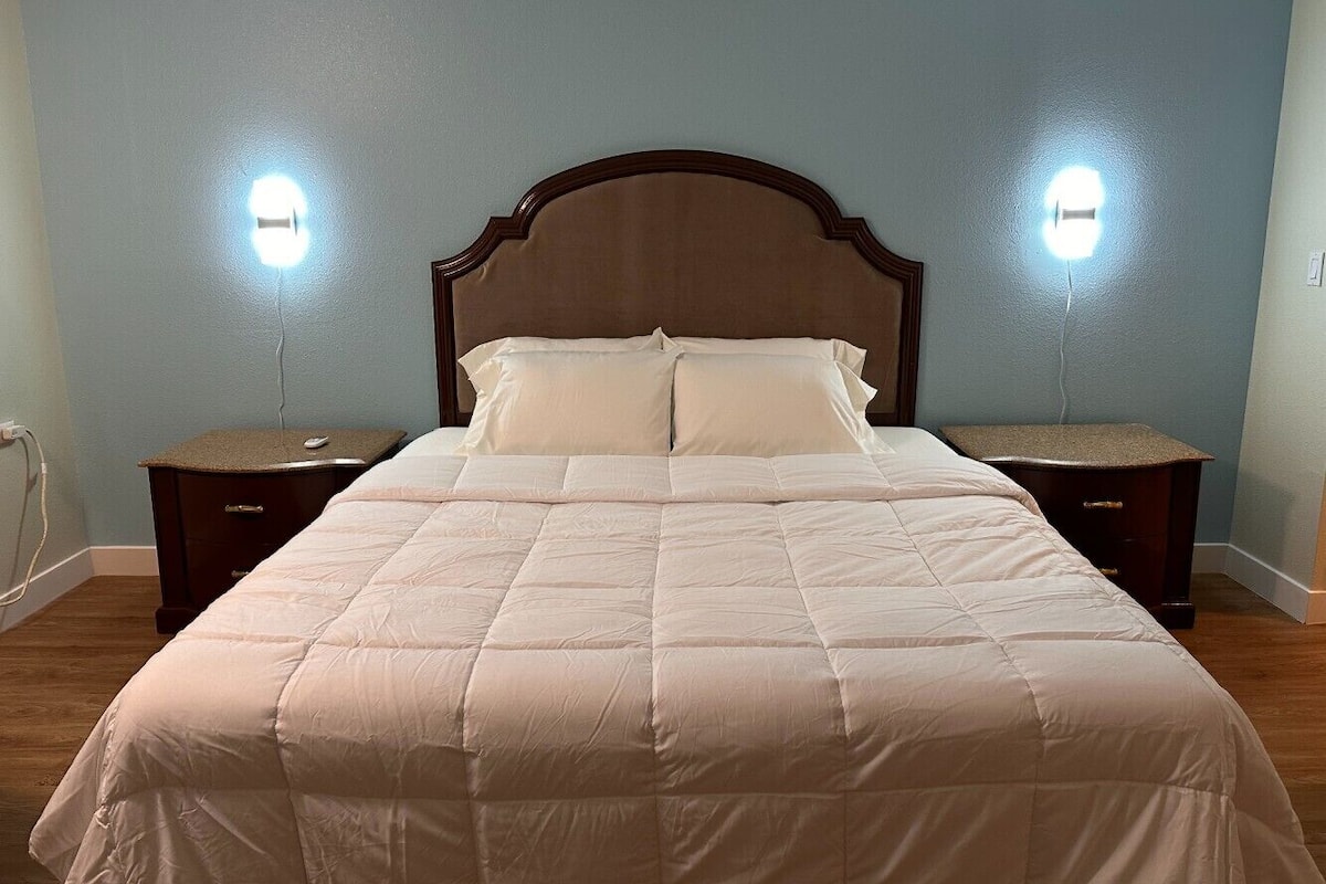 A neatly made bed with a wooden headboard, two bedside tables, and wall-mounted lights.
