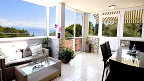 Ein sonnendurchfluteter Balkon mit Korbmöbeln, einem Glastisch und Blick aufs Meer.