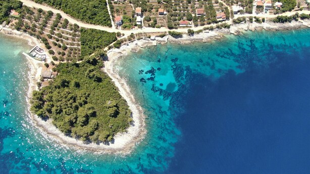 Ein Luftbild einer Küstenlandschaft mit einer kleinen Insel, umgeben von klarem türkisfarbenem Wasser.