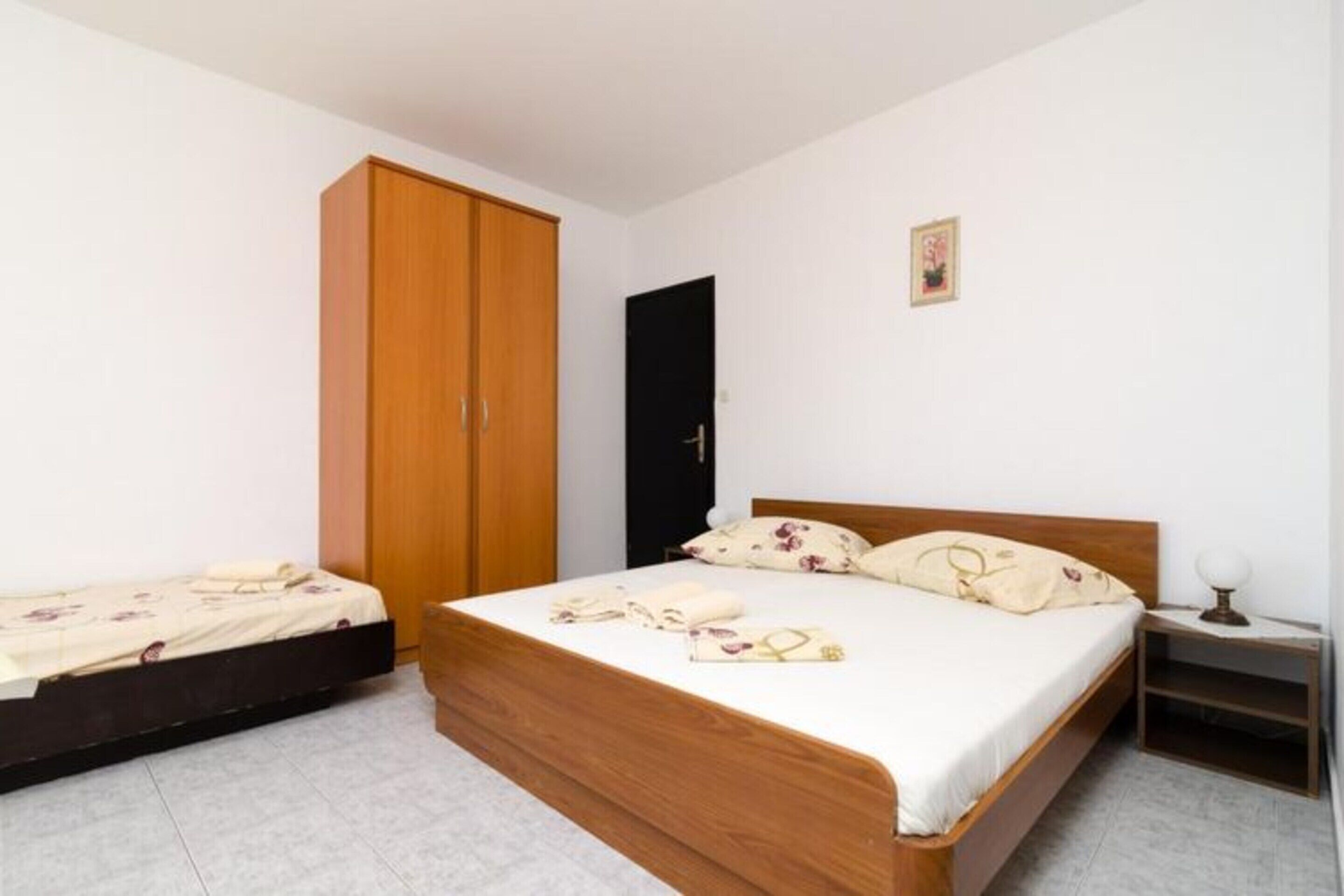A bedroom with a wooden bed, a smaller bed, a wardrobe, a nightstand, and a framed picture on the wall.
