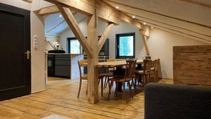 A dining area with a wooden table and chairs, a kitchen in the background, and a view of the outdoors through a window. - Spacious Holiday Home in Mayrhofen With hot tub (Mayrhofen)