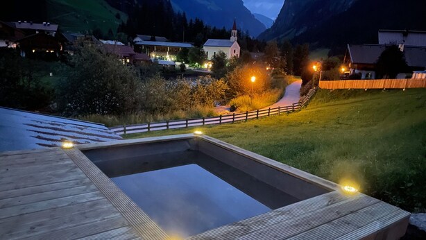 A wooden deck with a rectangular pool and surrounding lights, overlooking a village with buildings and a church. - Spacious Holiday Home in Mayrhofen With hot tub (Mayrhofen)