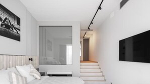 Ein modernes Schlafzimmer mit einem großen Bett, einem an der Wand montierten Fernseher und einer Treppe zu einem anderen Raum.
