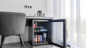 Ein modernes Zimmer mit grauem Sessel, einer Minibar mit Getränken und einer Kaffeemaschine.