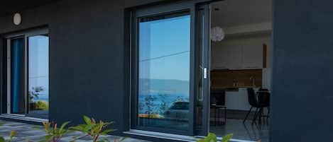 A modern building with large sliding glass doors leading to a kitchen area with white cabinets and a black countertop.