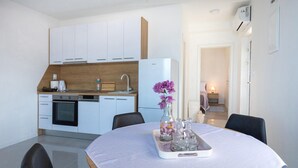 Una cocina moderna con armarios blancos, horno empotrado y refrigerador. Hay una mesa de comedor con un florero de flores moradas y saleros y pimenteros.