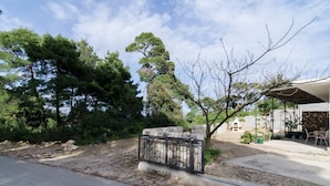 A paved driveway leading to a stone gate, surrounded by dense trees and a building with a covered patio area. - Apartments Skurla - One Bedroom Apartment With Terrace (Mljet)