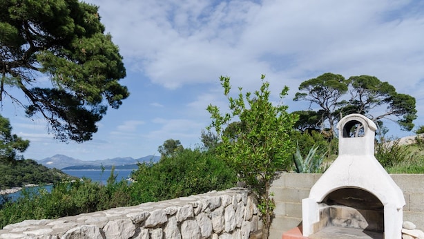 A stone wall and a stone oven with a view of the sea and mountains in the background. - Apartments Skurla - One Bedroom Apartment With Terrace (Mljet)