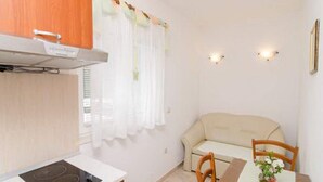 A compact kitchen with a stove, wooden cabinets, and a dining area with a table and chairs. - Apartments Skurla - One Bedroom Apartment With Terrace (Mljet)