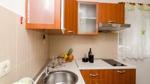 A kitchen with wooden cabinets, a stainless steel sink, and a window with a curtain. - Apartments Skurla - One Bedroom Apartment With Terrace (Mljet)