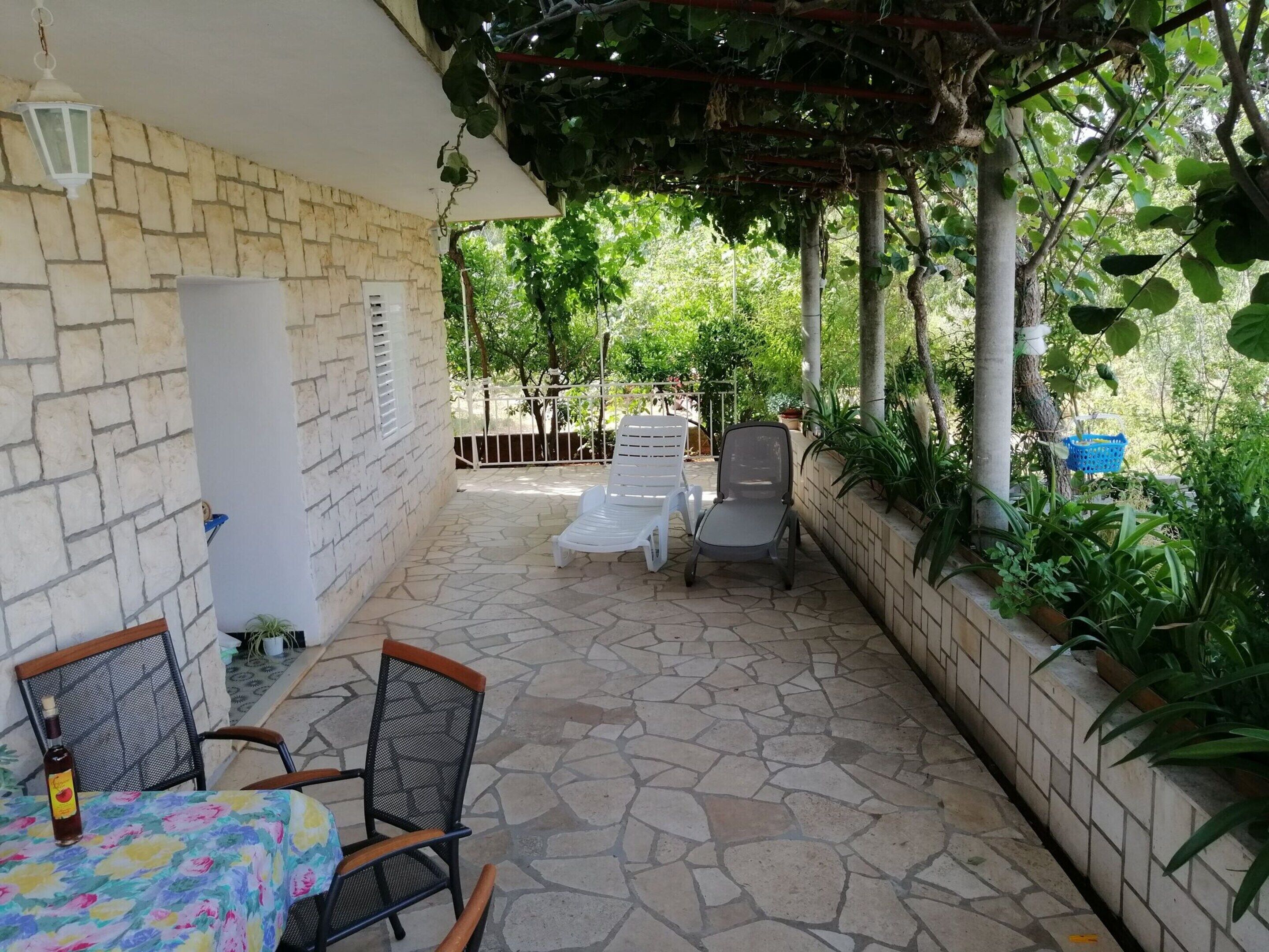 Un patio con suelo de piedra, una mesa con sillas, una pérgola cubierta de hiedra y vistas a un jardín.