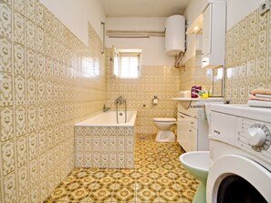 Um banheiro com ladrilhos estampados, banheira, vaso sanitário, máquina de lavar e pia.