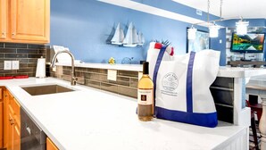 Uma cozinha com bancada branca, pia de aço inoxidável, armários de madeira e parede azul com arte de barcos à vela.