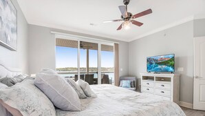 Een slaapkamer met een groot bed, een plafondventilator, een televisie en uitzicht op het omliggende landschap.