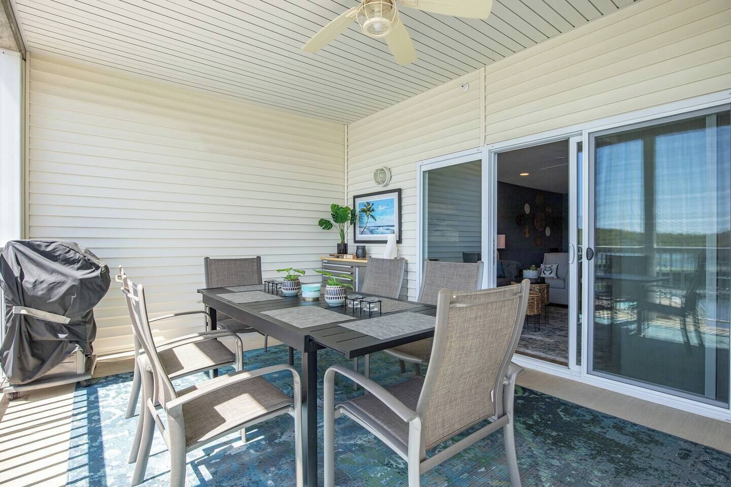 A covered patio with a table and chairs, a grill, and a sliding glass door leading to an interior space.