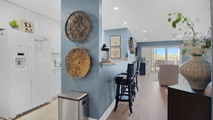A modern kitchen with white cabinets, a stainless steel trash bin, and decorative wall art. - WaterFront Getaway Parkview Bay! Lux Condo 3Pools! (Osage Beach)