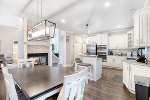 Une cuisine moderne avec des meubles blancs, un îlot central et un coin repas comprenant une table en bois foncé et des chaises blanches.
