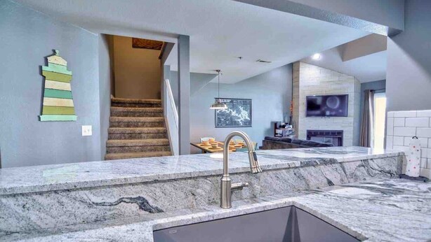 A modern kitchen with a granite countertop, a stainless steel sink, and a staircase leading to an upper level.