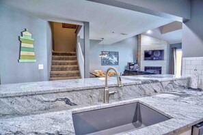 A modern kitchen with a granite countertop, a stainless steel sink, and a staircase leading to an upper level.
