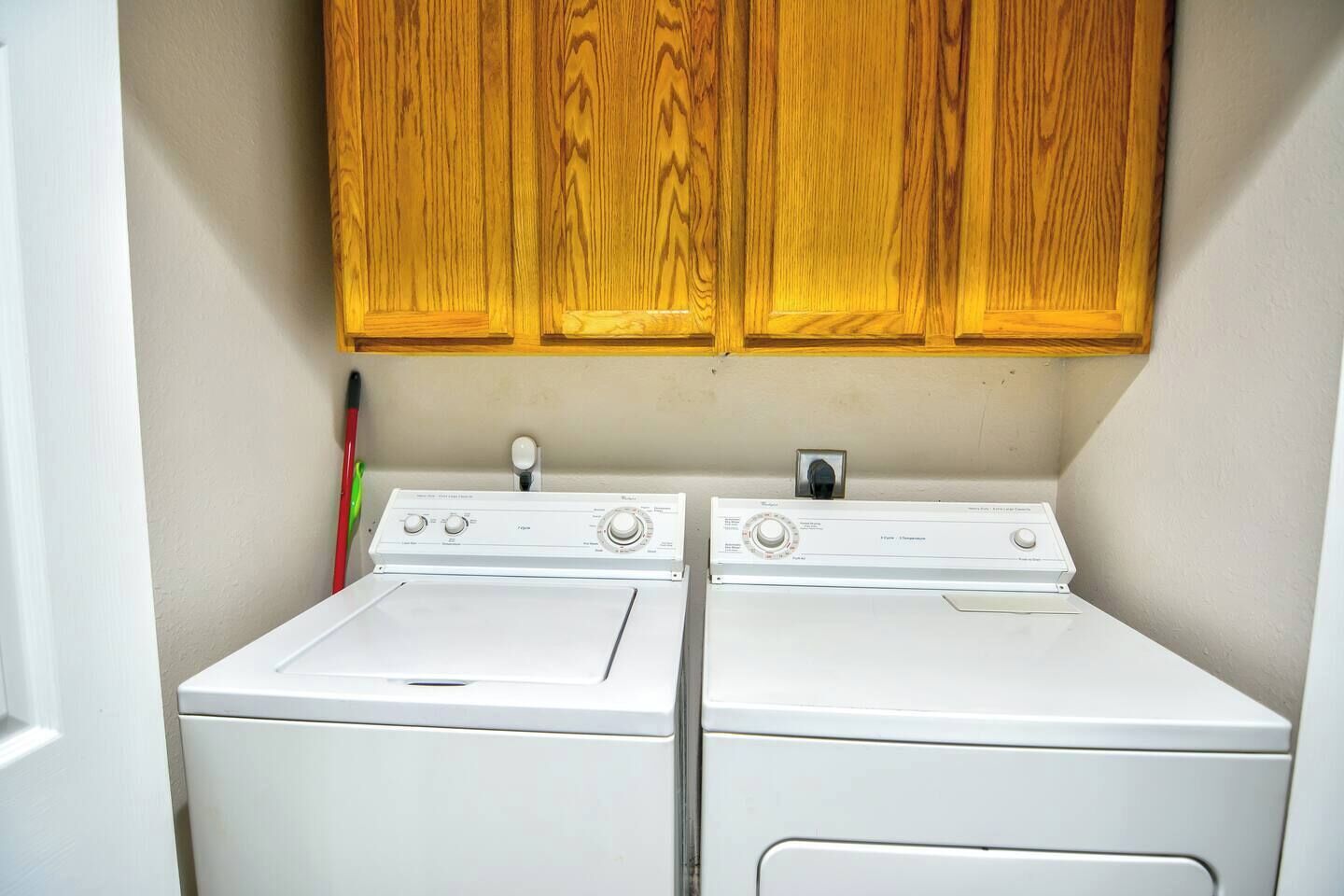 Een wasserette met twee witte wasmachines en houten kasten erboven.