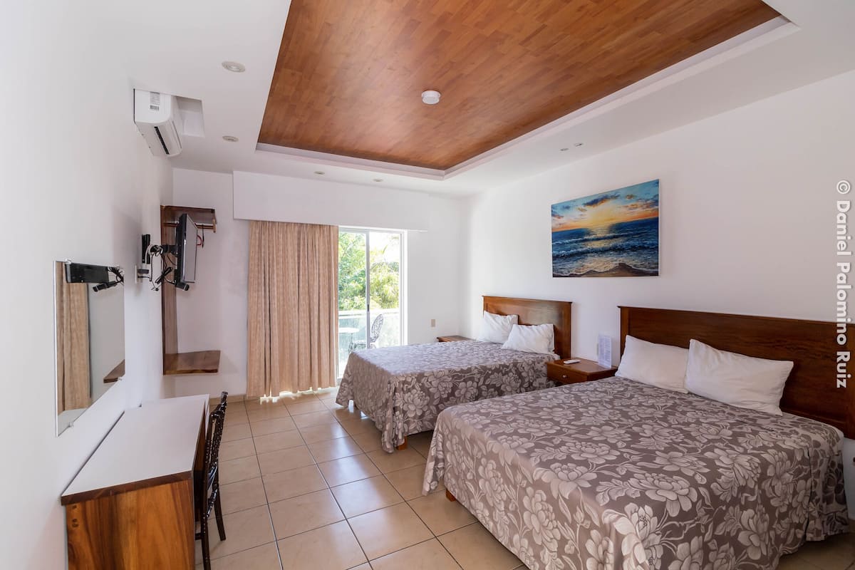 Habitación de hotel con dos camas, un escritorio y vistas al exterior.
