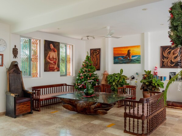 A spacious living room with a glass coffee table, wooden chairs, a Christmas tree, and various artworks on the walls. - Casa Pridda (Puerto Escondido)