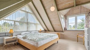 Ein Schlafzimmer mit schrägen Wänden, einem Bett, einem Nachttisch mit Lampe, einem Sessel und einem Kleiderschrank.
