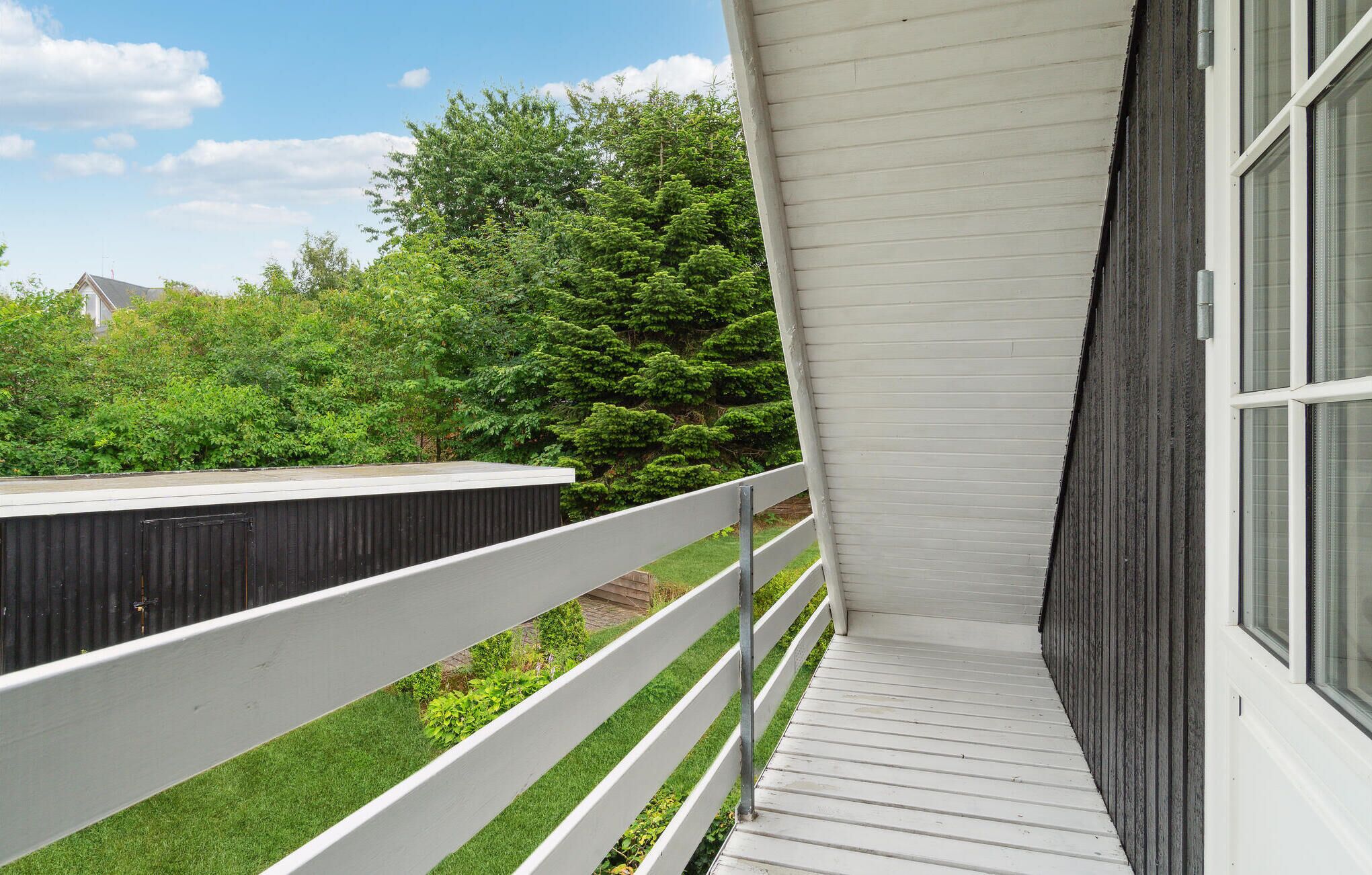 A balcony with a white railing, a grey awning, and a view of a green lawn and trees.