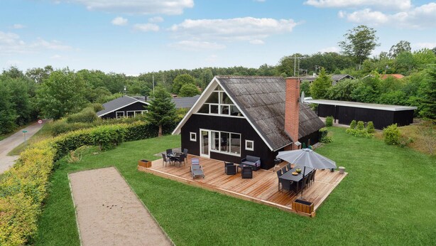 Ein modernes Haus mit einer großen Terrasse, einer überdachten Sitzgruppe im Freien und einem gepflegten Rasen.