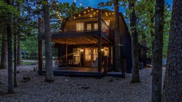 A cabin with a wooden deck and a covered porch, surrounded by trees.