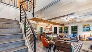 A spacious living area with a staircase, wooden beams, and modern furniture.