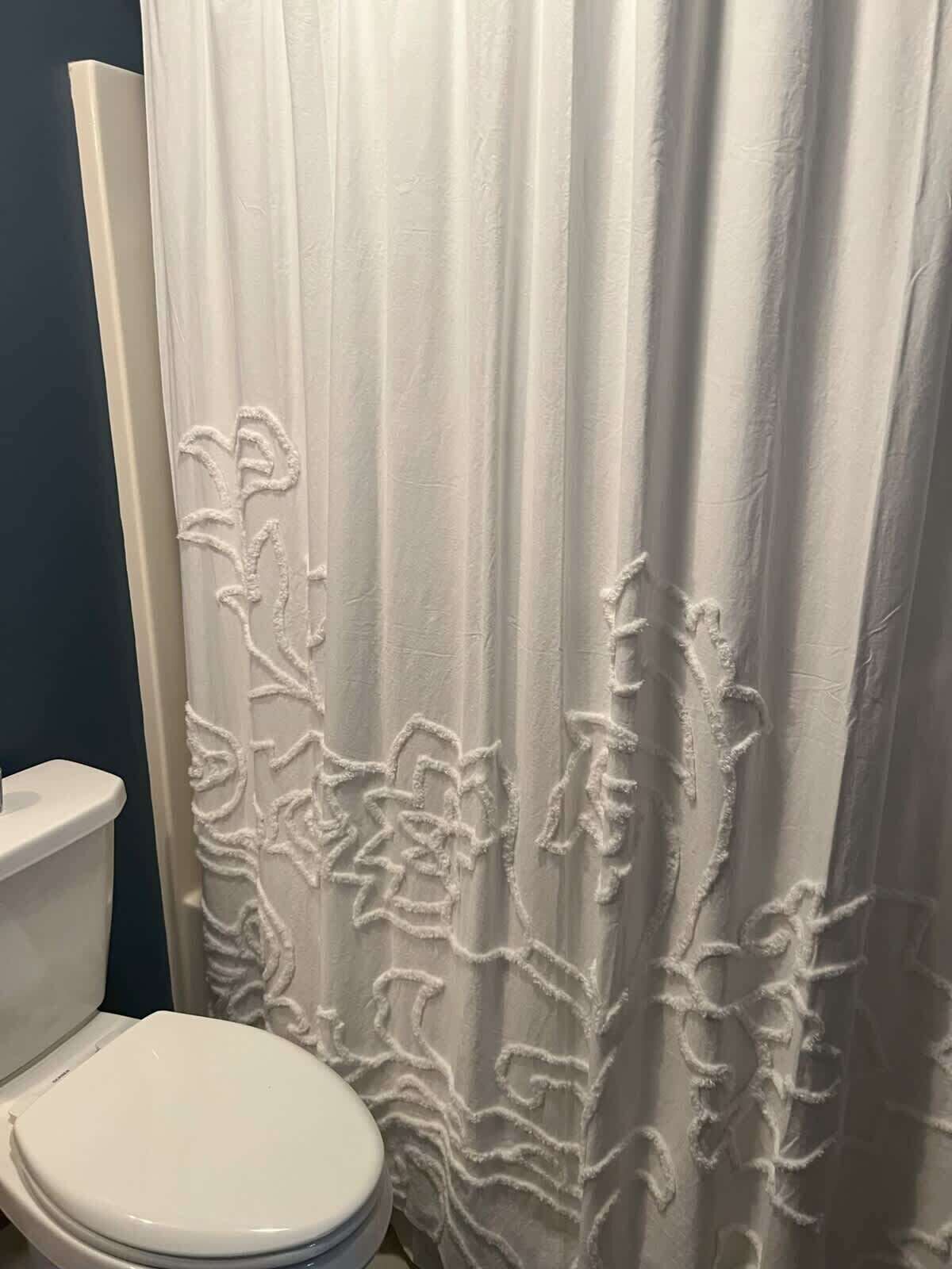 Ein Badezimmer mit einer weißen Toilette, einem Duschvorhang mit Blumenmuster und einer blauen Wand.