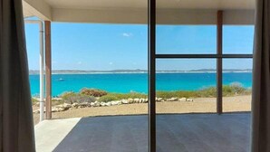 A room with a large sliding glass door leading to a balcony with a view of the sea and distant land.