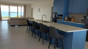 A modern kitchen with a central island, bar stools, and a view of the ocean.