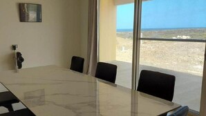 A conference room with a glass table and four chairs, a painting on the wall, and a view of a barren landscape through large windows.