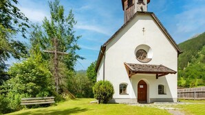 A small, white church with a bell tower, surrounded by lush greenery and a clear blue sky. - Modern Apartment in the Otztal (Oetz)