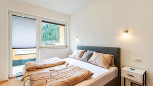 A bedroom with a bed, a nightstand, a wall-mounted light, and a window with blinds. - Modern Apartment in the Otztal (Oetz)