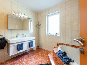 Ein Badezimmer mit weißem Waschtisch, einem großen Spiegel, einer Badewanne und einem Fenster.