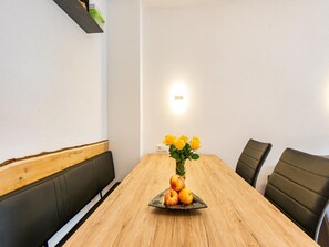 Ein Holztisch mit einer Fruchtschale und gelben Rosen, umgeben von Stühlen.