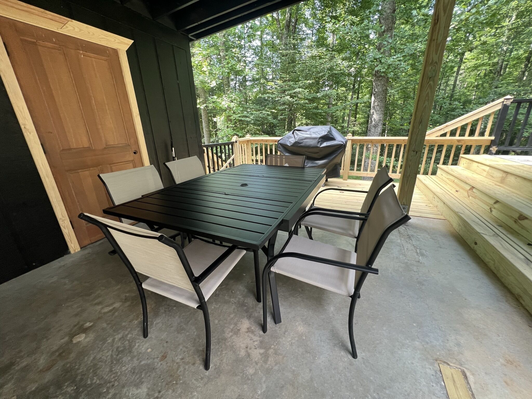 Un patio extérieur couvert, équipé d’une table et de chaises, d’un barbecue et d’une terrasse en bois.