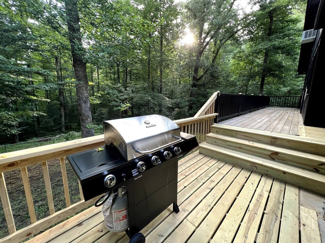 A barbecue grill on a wooden deck with a view of a forest.
