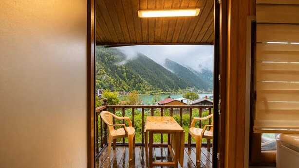 A wooden deck with a table and chairs, overlooking a mountainous landscape with a lake and buildings. - Uzungol Cerrahpasa Suites (Çaykara)