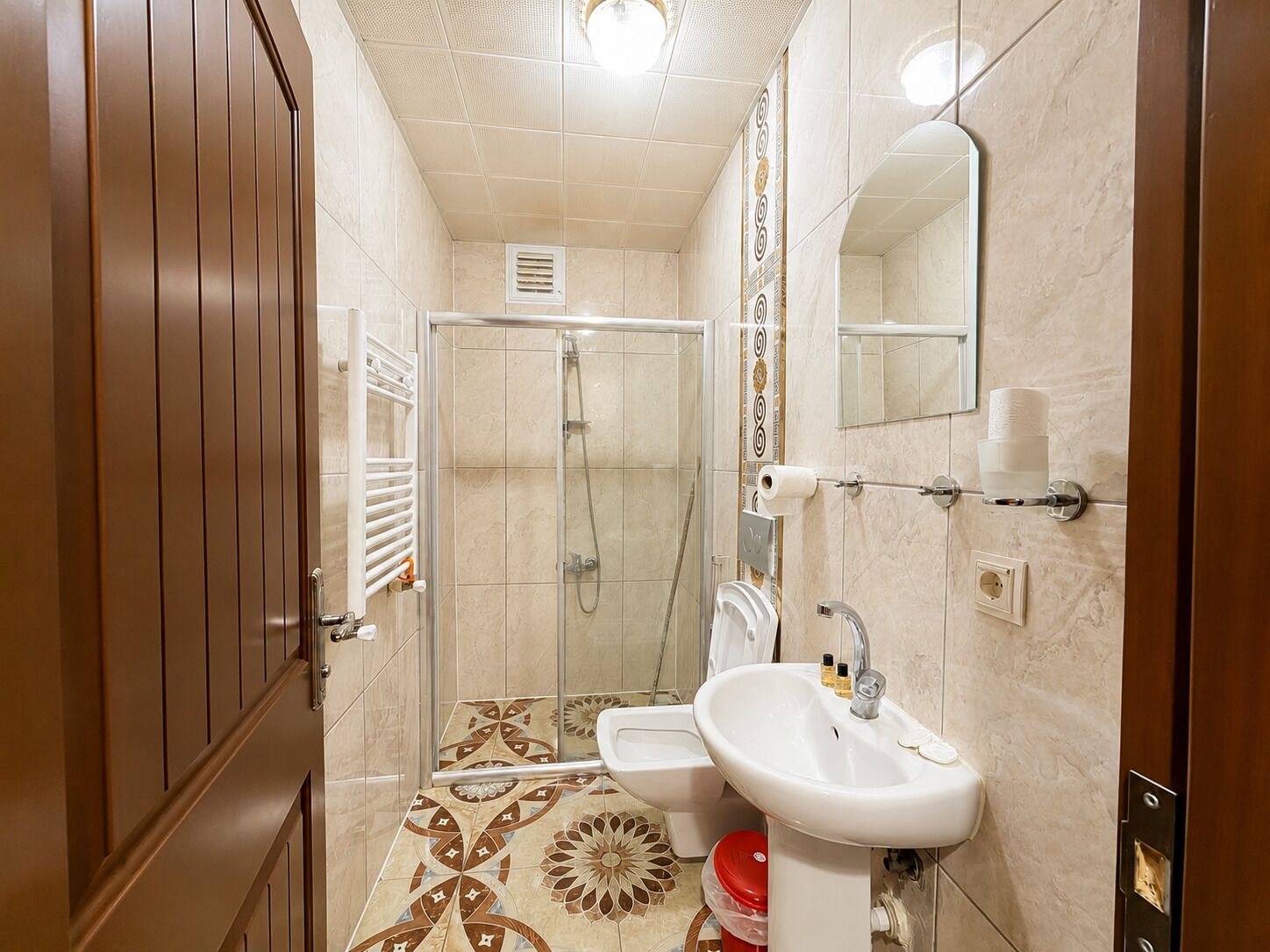 Un baño con ducha, dos lavamanos, inodoro y espejo.