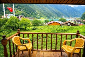 A wooden deck with two yellow chairs, overlooking a mountainous landscape with a lake and buildings. - Uzungol Cerrahpasa Suites (Çaykara)