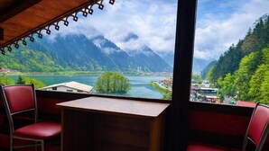 A room with a wooden desk and two red chairs, a large window with a view of a lake and mountains. - Uzungol Cerrahpasa Suites (Çaykara)