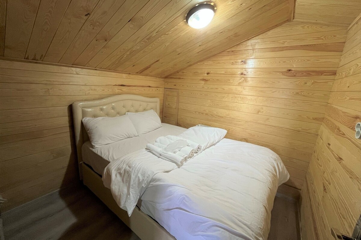 A wooden-paneled room with a bed, a ceiling light, and a wooden door.
