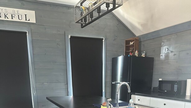 Una cocina moderna con una isla central, taburetes de bar, un lavamanos de acero inoxidable y un microondas.