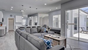 A modern living room with a sectional sofa, a coffee table, and a dining area. - Remodeled Golf Course Pool & Spa Home (Davenport)