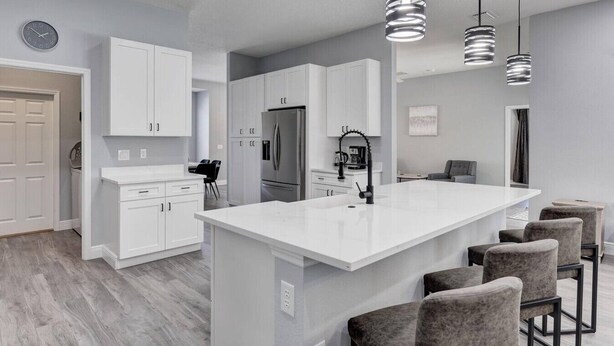 A modern kitchen with white cabinetry, a central island, and bar stools. - Remodeled Golf Course Pool & Spa Home (Davenport)