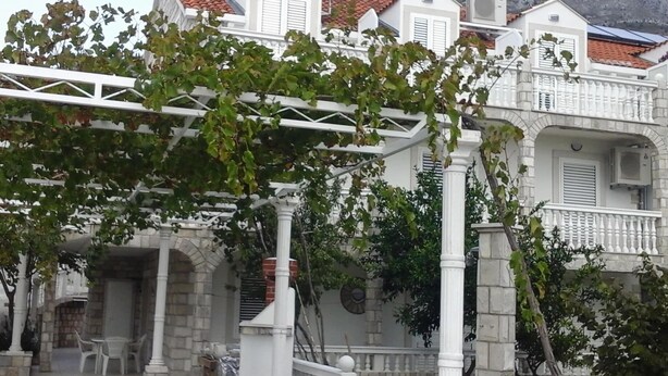 Een gebouw met een witte gevel, stenen zuilen en een overdekte patio met stoelen.